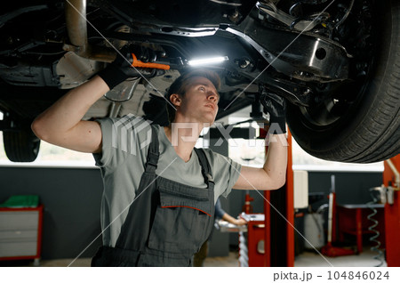 Male auto mechanic working under car lifted on elevator with flashlight Male auto mechanic working under car lifted on elevator with flashlight 104846024
