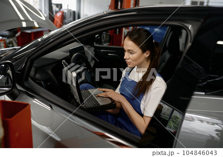 Woman technician sitting in car working on laptop providing computer diagnostics Woman technician sitting in car working on laptop providing computer diagnostics 104846043