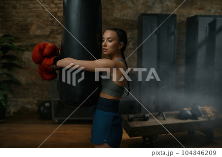 Young female boxer fighter hugging punching bag after intense workout Young female boxer fighter hugging punching bag after intense workout 104846209