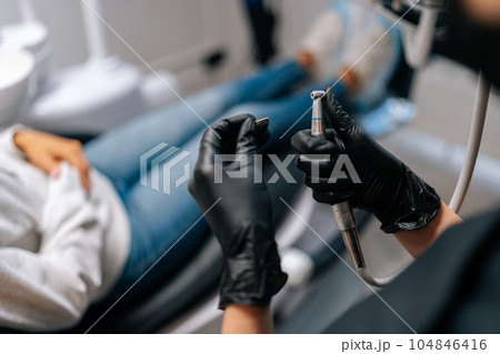 Closeup rear view of unrecognizable female dentist in gloves change drill into tool for treating caries on teeth. Close-up of doctor inserting polishing nozzle in dental bur. Dental equipment concept. 104846416