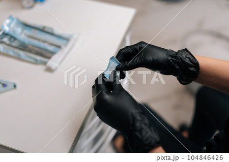 Close-up cropped top view of unrecognizable dentist in protective gloves opening package with new nozzle for polishing and grinding teeth of patient. Concept of teeth whitening, dental treatment. 104846426
