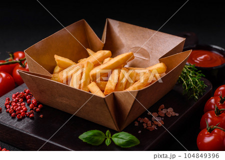 Delicious crispy french fries with salt and spices in a cardboard box 104849396