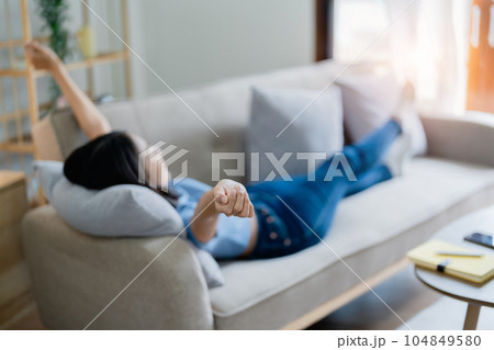 Home lifestyle woman relaxing sleeping on sofa patio living room. Happy lady lying down on comfortable pillows taking a nap for wellness and health. Tropical vacation 104849580