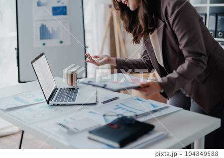 Portrait of a thoughtful Asian businesswoman looking at financial statements and making marketing plans using a computer on her desk. 104849588