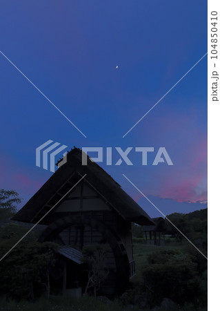 北杜市武川町、水車小屋の上、夕焼け雲の中に浮かぶ月齢5.9の月 104850410