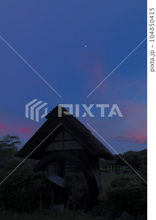 北杜市武川町、水車小屋の上、夕焼け雲の中に浮かぶ月齢5.9の月 104850415