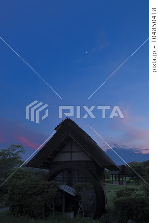 北杜市武川町、水車小屋の上、夕焼け雲の中に浮かぶ月齢5.9の月 104850418