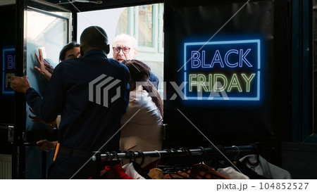 Diverse people demanding store access on black friday, trying to get inside of fashion boutique before opening hours. Anxious mad crowd fighting and arguing with security guard at entrance. 104852527