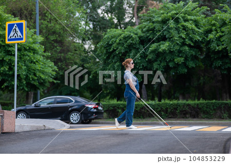 Blind pregnant woman crosses the road at a crosswalk with a cane. Blind pregnant woman crosses the road at a crosswalk with a cane. 104853229