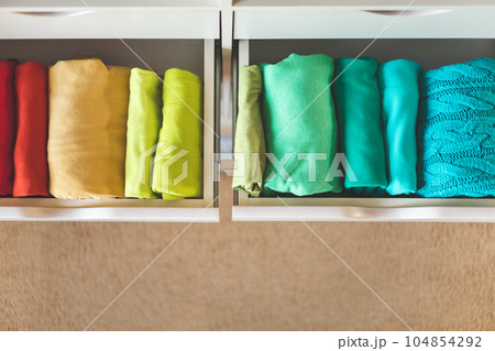 Multi-colored clothes folded vertically in a wardrobe drawer. The concept of order and storage Multi-colored clothes folded vertically in a wardrobe drawer. The concept of order and storage 104854292
