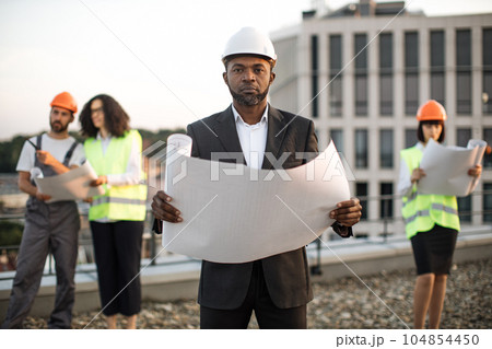 Investor posing at camera while colleagues inspecting object 104854450