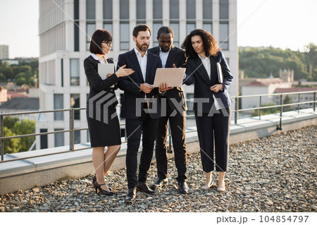 Specialists watching online webinar on laptop outdoors Specialists watching online webinar on laptop outdoors 104854797