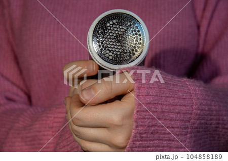 Woman using Anti-pilling razor at home. Device for shaving clothes. Anti-Plush fabric Shaver. Electric portable sweater pill defuzzer Lint remover from pink acrylic or wool sweater. Slow fashion Woman using Anti-pilling razor at home. Device for shaving clothes. Anti-Plush fabric Shaver. Electric portable sweater pill defuzzer Lint remover from pink acrylic or wool sweater. Slow fashion 104858189