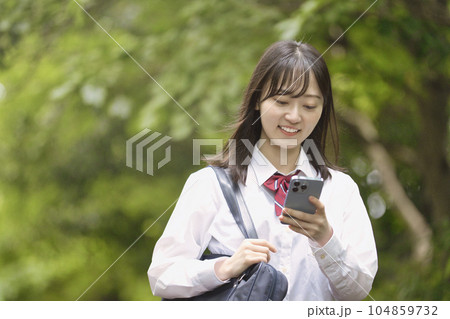 新緑の中スマホを持つ女子高生 104859732
