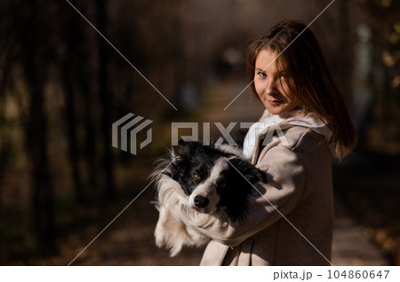 Caucasian woman holding a border collie in her arms while walking in the autumn park. Portrait of a girl with a dog. 104860647