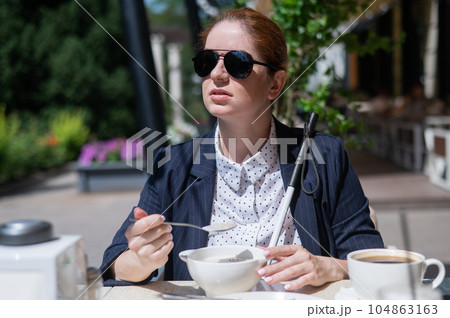 Blind caucasian woman in suit eating porridge for breakfast in outdoor cafe.  104863163
