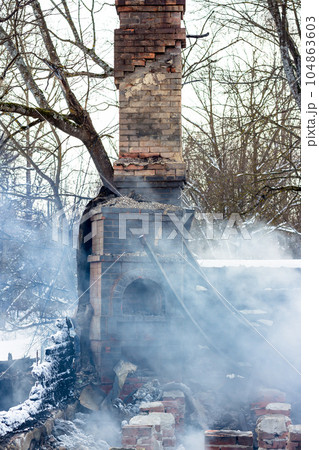 Remains of a house after a fire. The brick tube of the stove is shrouded in dense smoke. A vertical view of the gloomy ash 104863603
