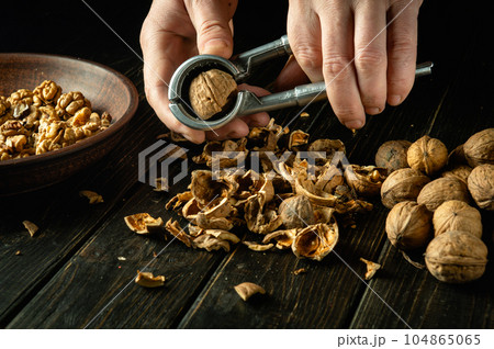 Peeling nuts with a nutcracker by the hands of a cook. Peeled walnuts in a plate and on the kitchen table Peeling nuts with a nutcracker by the hands of a cook. Peeled walnuts in a plate and on the kitchen table 104865065