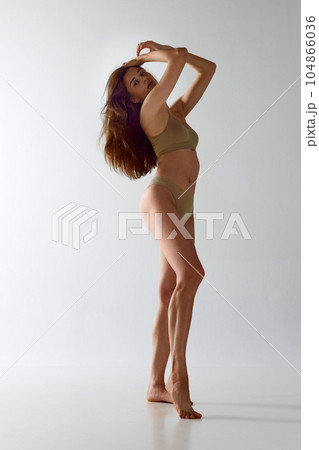 Full-length portrait of tender young woman with fit, slim body standing in underwear against grey studio background 104866036