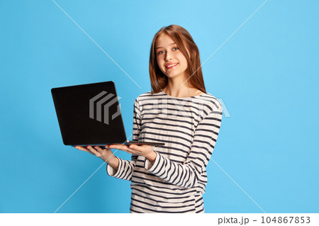 Job fair. Young pretty girl standing with laptop and smiling against blue studio background. Employment 104867853