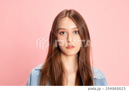 Portrait of young beautiful woman looking at camera with calm, serious expression against pink studio background 104868025