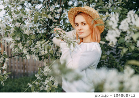 Portrait of a woman in a straw hat in a cherry blossom. Free outdoor recreation, spring blooming garden. 104868712