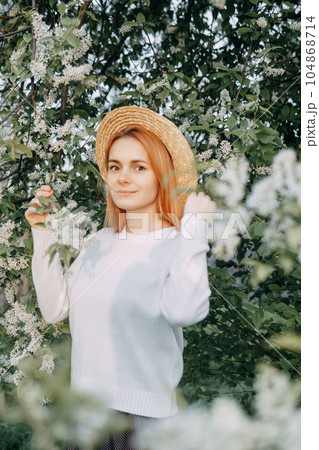 Portrait of a woman in a straw hat in a cherry blossom. Free outdoor recreation, spring blooming garden. 104868714