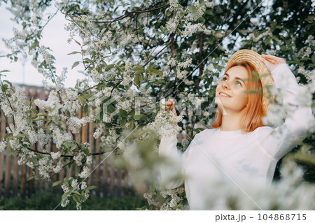 Portrait of a woman in a straw hat in a cherry blossom. Free outdoor recreation, spring blooming garden. 104868715