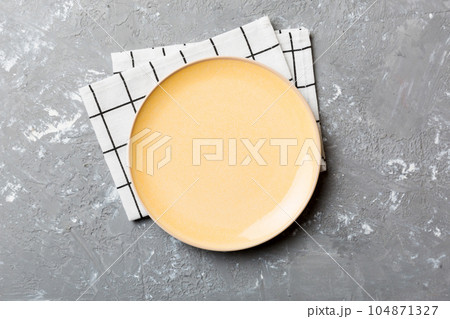 Top view on colored background empty round yellow plate on tablecloth for food. Empty dish on napkin with space for your design 104871327