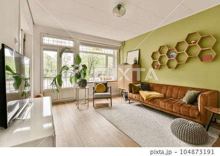 a living room with green walls and wood flooring the room has a brown leather couch, two chairs, a flat screen tv 104873191
