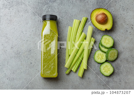 Bottle of green vegetable smoothie with fresh celery sticks, cut avocado, cucumber on gray concrete background top view. Diet beverage, healthy nutrition, detox concept 104873207