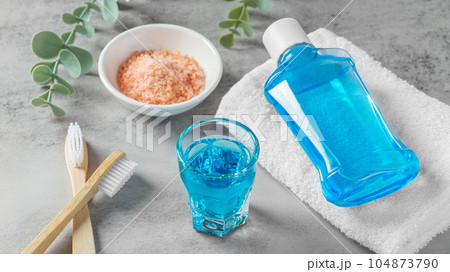 Mouthwash in glass and toothbrush with pink salt on grey table, teeth care Mouthwash in glass and toothbrush with pink salt on grey table, teeth care 104873790
