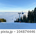 Ski Resort evening with lots of snow and clouds stretch to the horizon view. Mountain Lift moves through clouds. 104874446