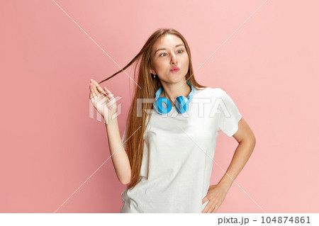 Portrait of young beautiful girl in casual clothes and headphones posing with grimacing funny face against pink studio background. 104874861