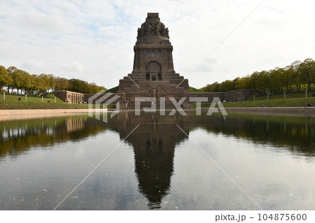 Pond reflecting the Monument to the Battle of the Nations in Leipzig, Germany against a cloudy sky 104875600