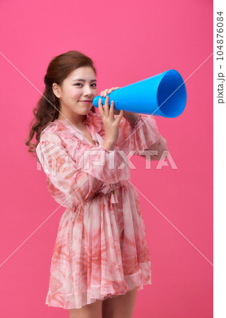female model wearing a flower-patterned dress with a pink background and using a blue loudspeaker 104876084