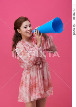 female model wearing a flower-patterned dress with a pink background and using a blue loudspeaker 104876086