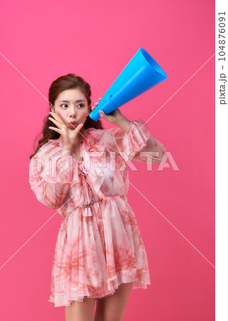 female model wearing a flower-patterned dress with a pink background and using a blue loudspeaker 104876091