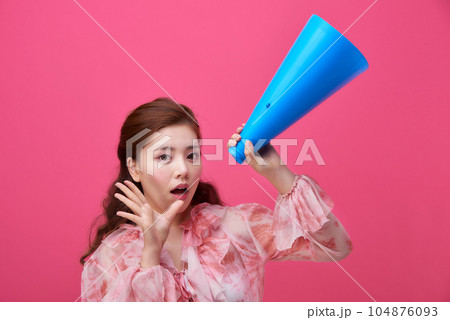female model wearing a flower-patterned dress with a pink background and using a blue loudspeaker 104876093