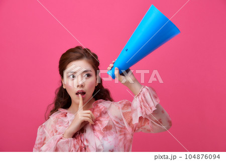 female model wearing a flower-patterned dress with a pink background and using a blue loudspeaker 104876094