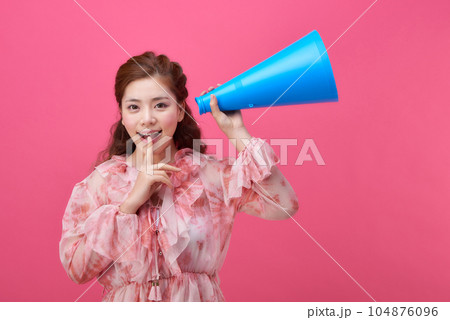 female model wearing a flower-patterned dress with a pink background and using a blue loudspeaker 104876096