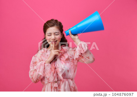 female model wearing a flower-patterned dress with a pink background and using a blue loudspeaker 104876097