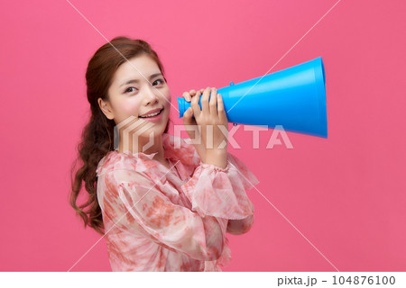 female model wearing a flower-patterned dress with a pink background and using a blue loudspeaker 104876100