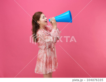 female model wearing a flower-patterned dress with a pink background and using a blue loudspeaker 104876105