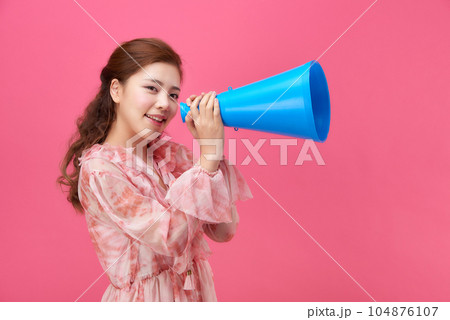 female model wearing a flower-patterned dress with a pink background and using a blue loudspeaker 104876107