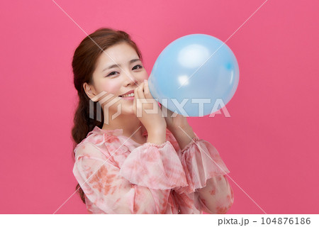 female model wearing a flower-patterned dress with a pink background and blowing blue balloons 104876186