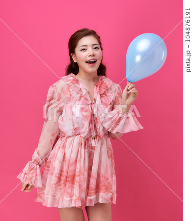 female model wearing a flower-patterned dress with a pink background and blowing blue balloons 104876191