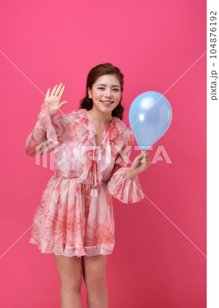 female model wearing a flower-patterned dress with a pink background and blowing blue balloons 104876192