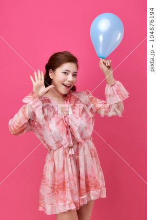 female model wearing a flower-patterned dress with a pink background and blowing blue balloons 104876194