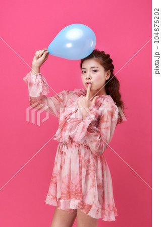 female model wearing a flower-patterned dress with a pink background and blowing blue balloons 104876202